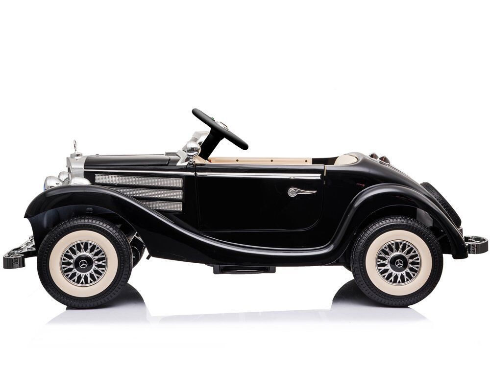 Schwarzes Elektro-Kinderauto im Oldtimer-Stil, seitlich auf weißem Hintergrund. Mit verchromten Stoßstangen und markantem Kühlergrill. Cremefarbene Reifen mit schwarzen Speichenfelgen, beiges Interieur mit Lenkrad und Sitz.