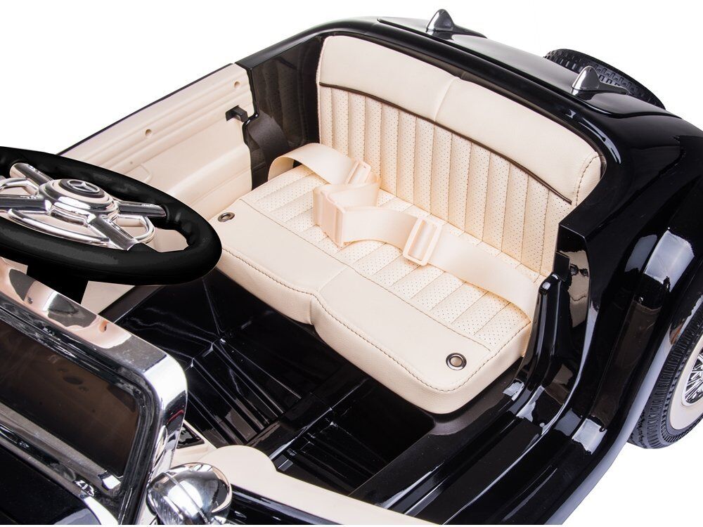 Interieur eines schwarzen Kinderautos mit beigem perforiertem Sitz und Sicherheitsgurt. Zu sehen sind schwarzes Lenkrad mit Chromdetails, glänzendes Armaturenbrett und Beifahrerseite. Chromakzente betonen den Look.