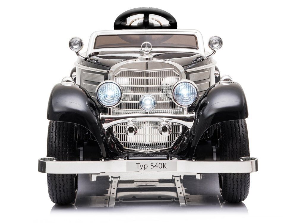 Schwarzer Kinder-Sportwagen im Stil eines klassischen Mercedes 540K, frontal. Chromgrill, Haupt- und Zusatzscheinwerfer, verchromte Stoßfänger, schwarze Kotflügel, dunkles Lenkrad, weißer Hintergrund.