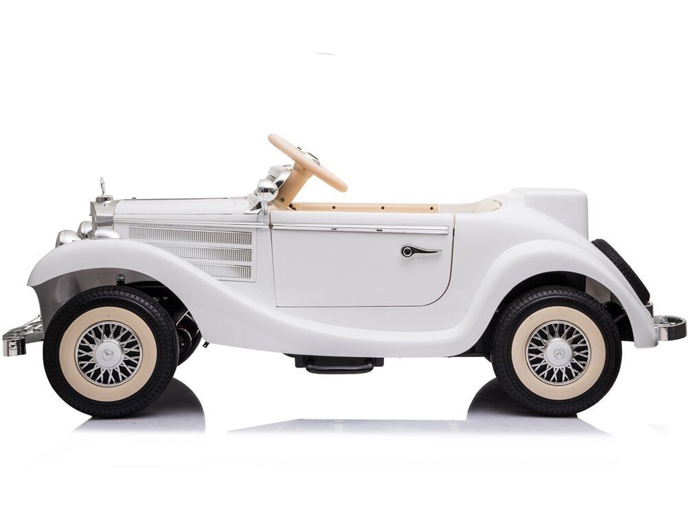 Weißes Kinder-Elektroauto im klassischen Oldtimerstil, seitlich. Elegante geschwungene Kotflügel, chromglänzender Kühlergrill und Scheinwerfer, beigefarbene Reifenflanken, Holzlenkrad, Reserverad am Heck. Auf reflektierendem Weiß.