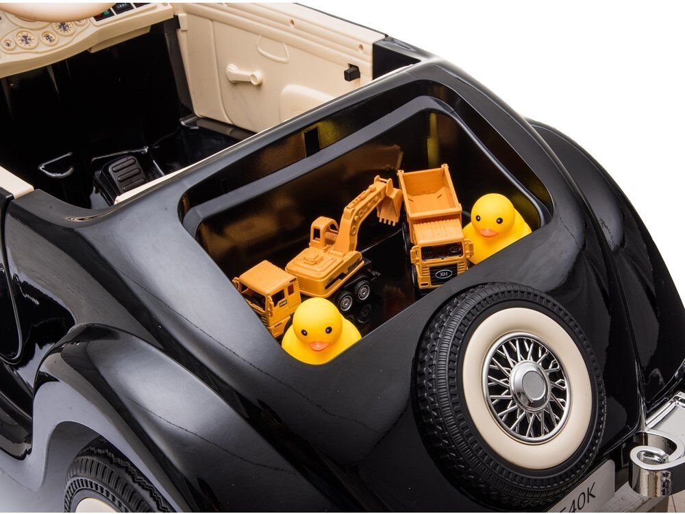 Schwarzes, glänzendes Retro-Kinderspielzeugauto mit cremefarbenen Sitzen. Im Innenraum: zwei gelbe Quietscheentchen, ein orangefarbener Spielzeugbagger und ein kleiner Lastwagen. Hinten Ersatzrad mit weißer Abdeckung.
