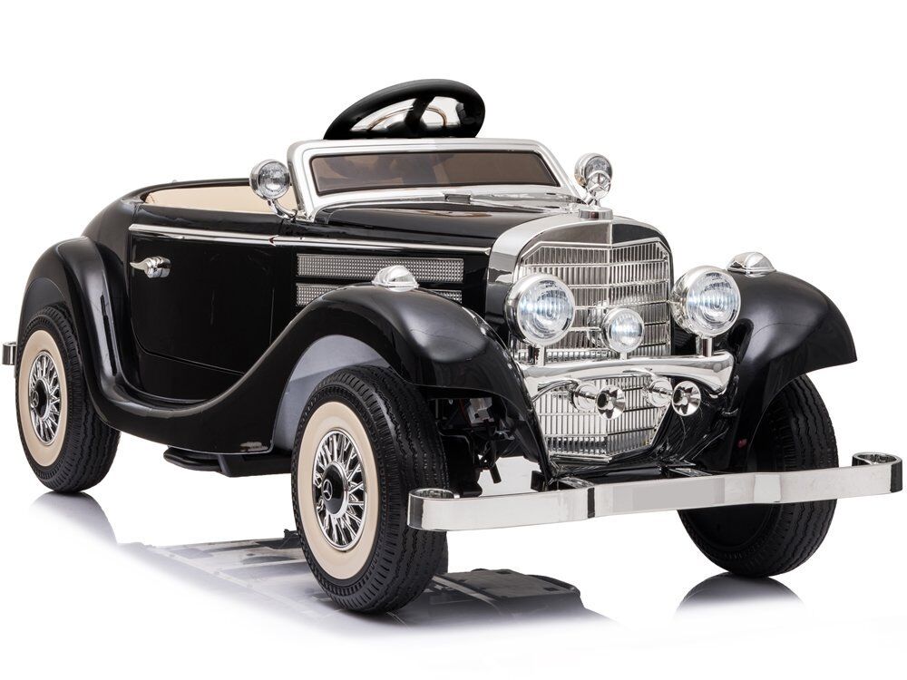 Schwarzes Spielzeug-Oldtimerauto, schräg gesehen: Chromgrill, vier runde Scheinwerfer, verchromte Stoßstangen/Zierleisten, Weißwandreifen mit silbernen Felgen, heller Innenraum, schwarzes Lenkrad.